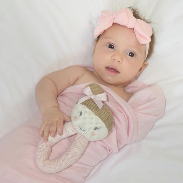 Baby-girl-with-ballerina-rattle-and-blush-muslin-swaddle-wrap-web-grande