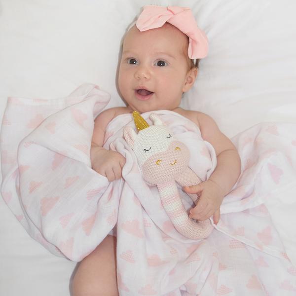 Baby-girl-with-unicorn-rattle-and-blush-cloud-muslin-swaddle-web-grande